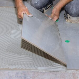 person installing tile to floor using adhesive